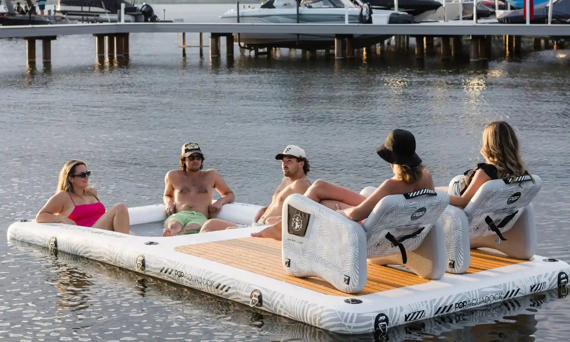 Group relaxing on POP AquaDock inflatable dock with chairs on the water.